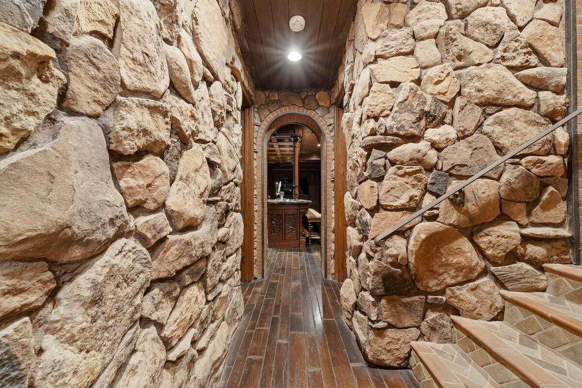 Stone-walled hallway with wood floors leading to the Irish pub-style basement bar in the Foothills Village Drive home