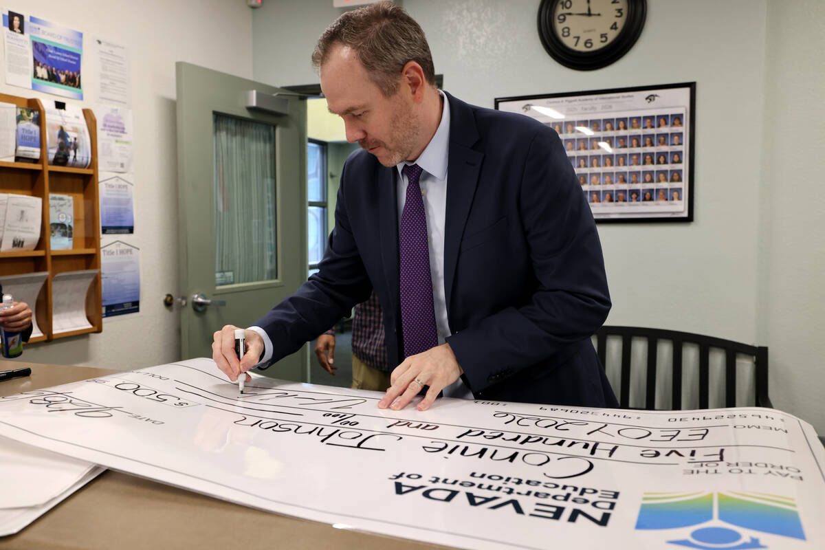 Nevada Superintendent of Public Instruction Dr. Victor Wakefield signs a $500 check before the surprise award ceremony for Piggott Academy preschool teacher Connie Johnson