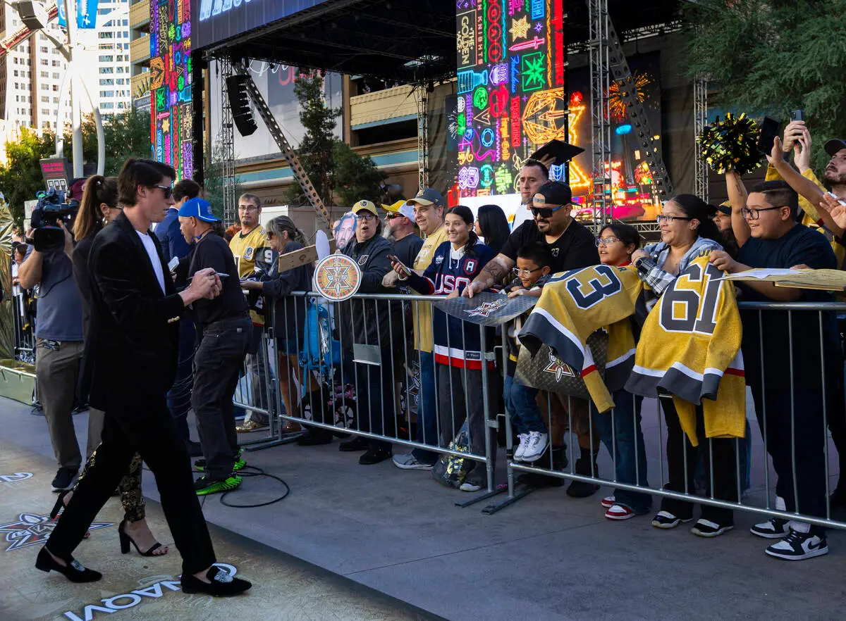 A Golden Knights player in a black suit walks past a railing of fans in jerseys and waves under clear skies on the gold carpet at Paramount+ Plaza before the Season X opener on Sept. 29, 2026