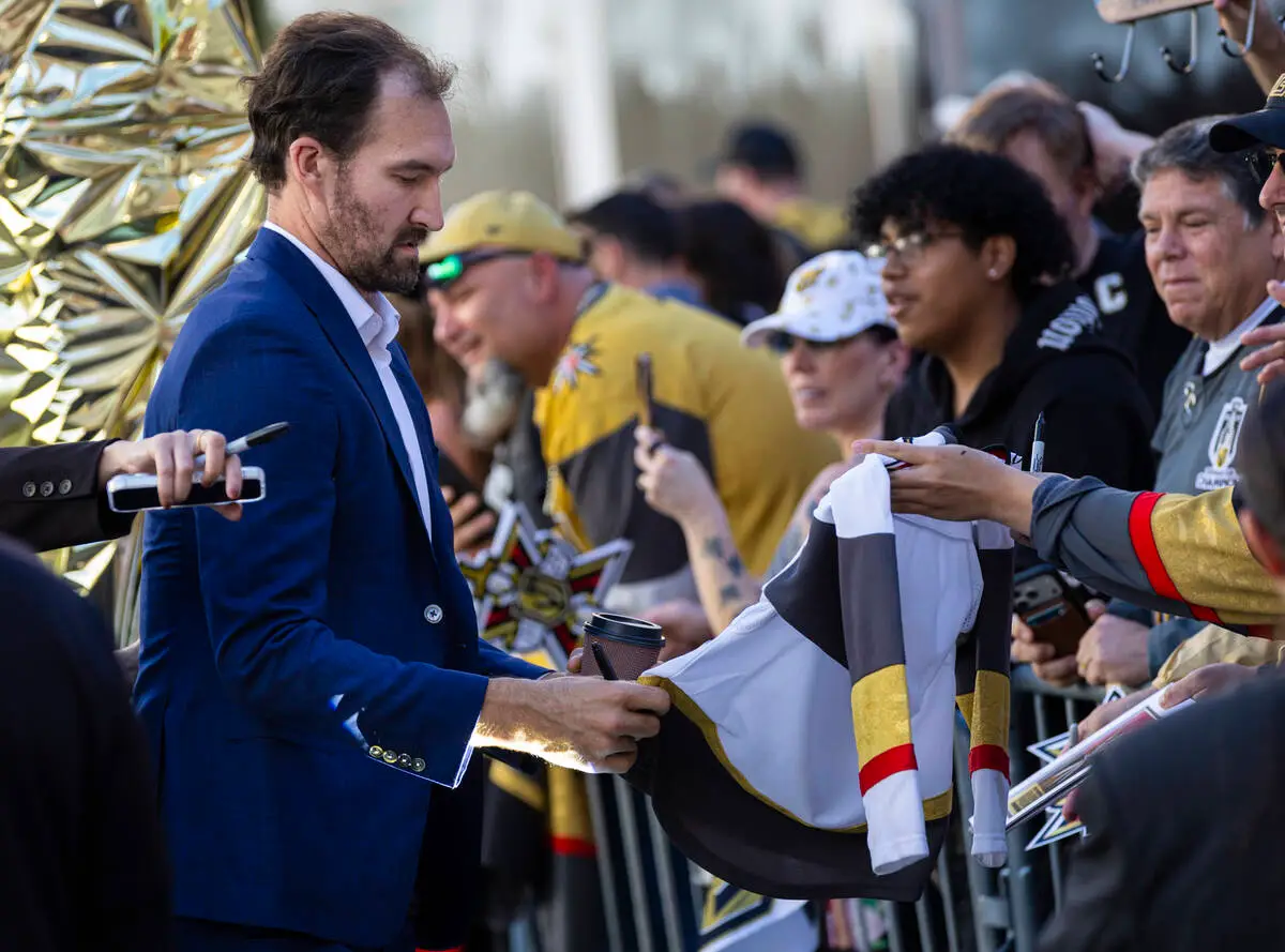 A Golden Knights player in a blue suit signs a white Golden Knights jersey held over the rail by a fan on the gold carpet before the season opener against the Chicago Blackhawks