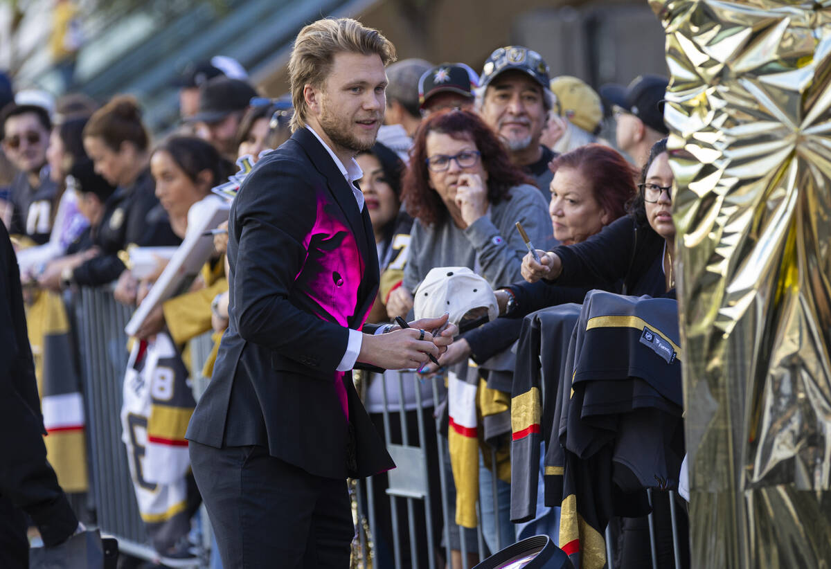 A Golden Knights player with blond hair in a black and pink jacket shakes hands with fans along the barricade next to the gold decorations at Paramount+ Plaza