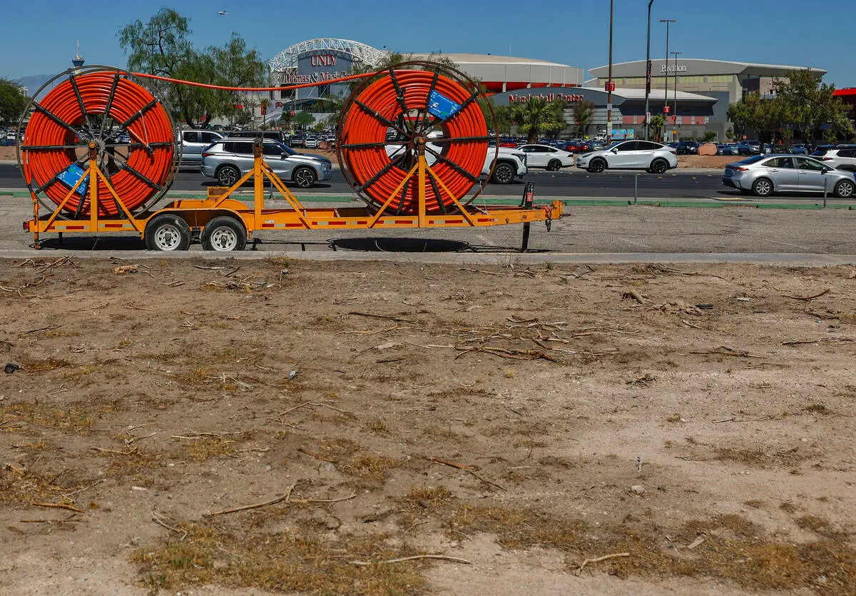 Cable spools on a trailer beside the cleared former UNLV Paradise Campus site, with the Thomas and Mack Center in the background